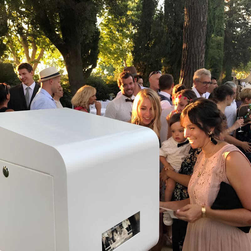 Des invités récupèrent leurs photos à la sortie de la borne pendant un cocktail en plein air